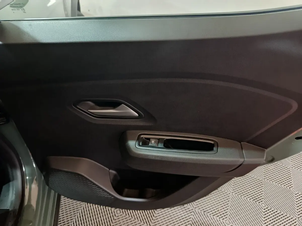 Vue rapprochée de la porte avant gauche verte de la Dacia Sandero Extreme+ TCe 110 avec poignée intérieure et commande de vitre.