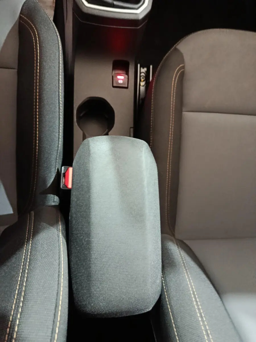 Vue plongeante sur l'accoudoir central et les sièges avant gris avec surpiqûres orange de la Dacia Sandero 2024.