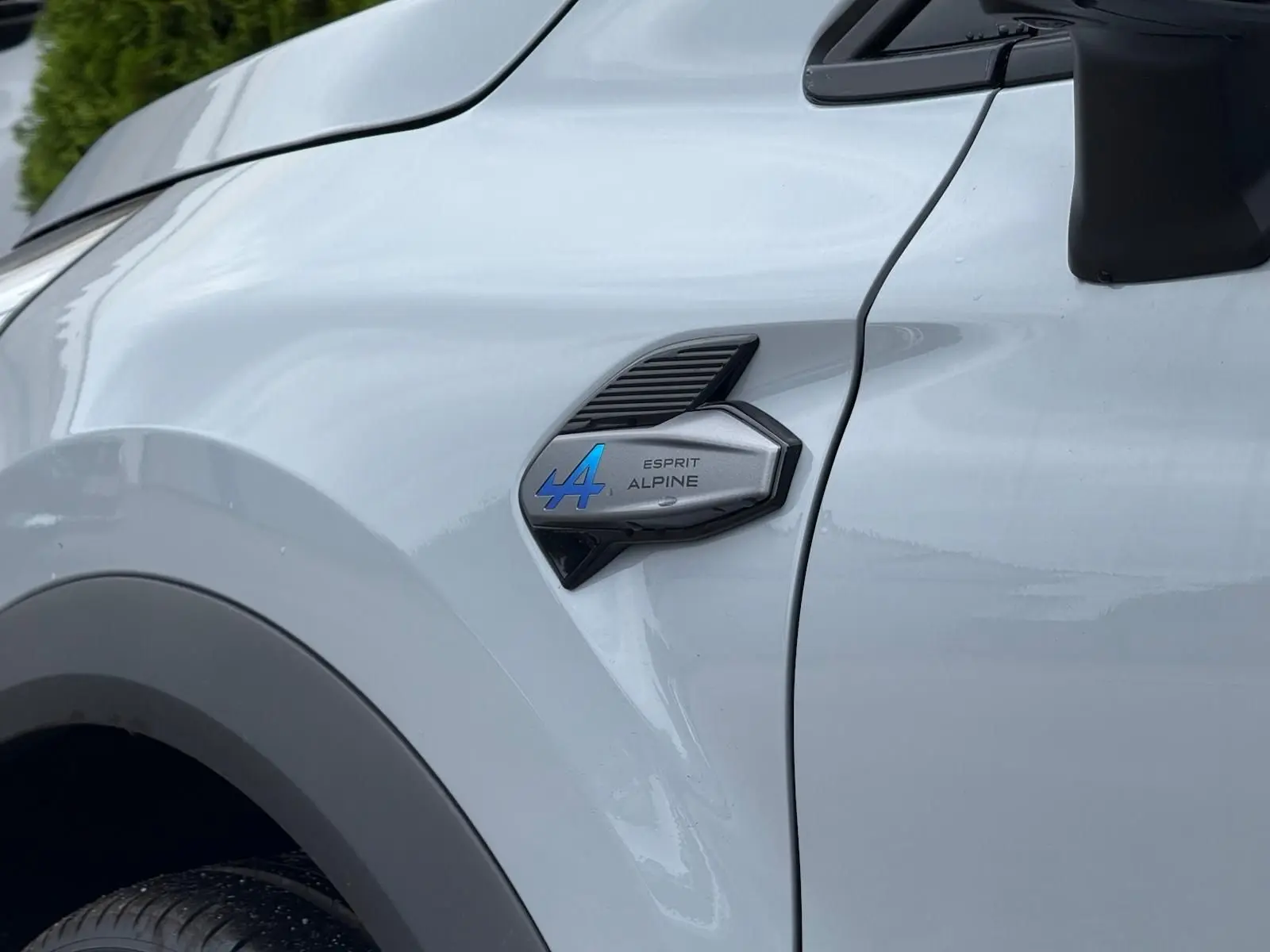 Gros plan sur l'aile avant gauche grise Rafale du Renault Symbioz 2026 avec logo Esprit Alpine bleu et noir.