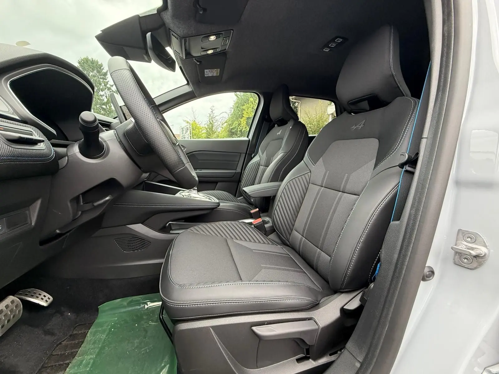 Vue intérieure côté conducteur de la Renault Symbioz gris rafale, sièges sport noirs avec surpiqûres bleues et volant cuir.