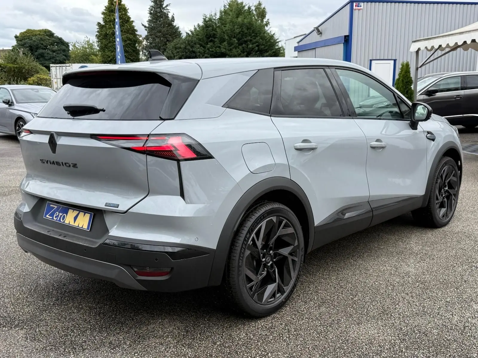 Vue 3/4 arrière droit d'une Renault Symbioz gris rafale avec jantes noires et feux arrière LED distinctifs.