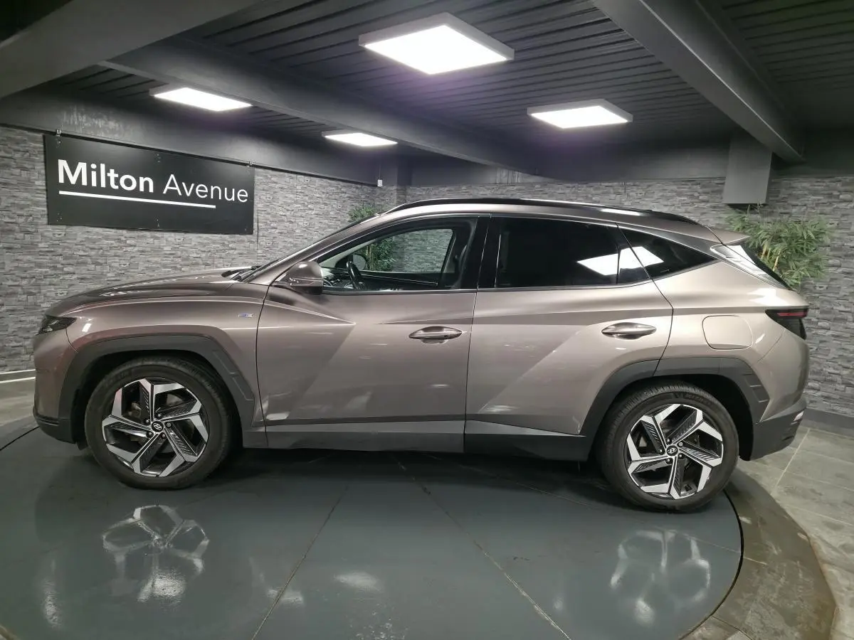 Vue de profil côté gauche d'un Hyundai Tucson gris métallisé avec jantes alliage et vitres teintées dans un showroom.