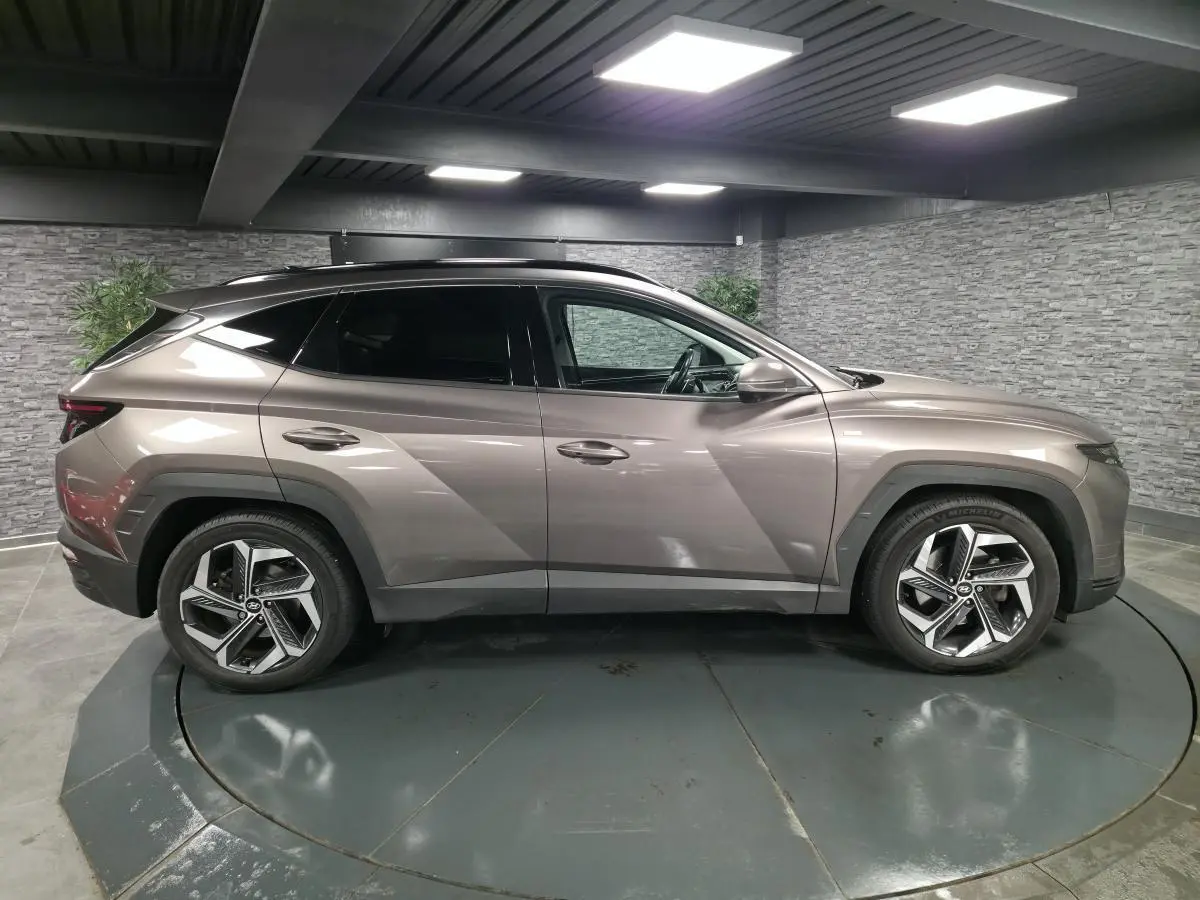 Vue latérale droite d'un Hyundai Tucson gris métallisé avec jantes alliage et vitres teintées en intérieur fermé.