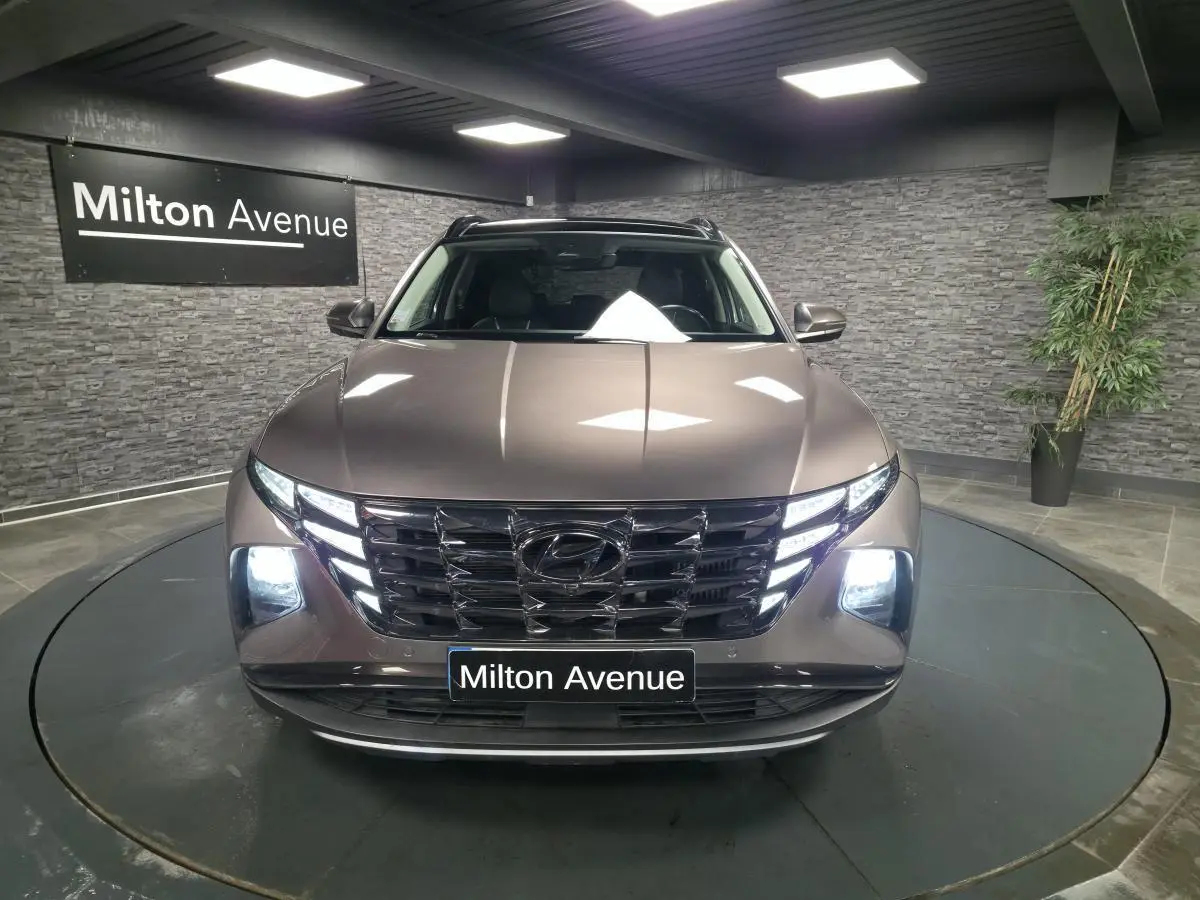 Vue avant d’un Hyundai Tucson gris métallisé avec calandre chromée et feux LED allumés en showroom.