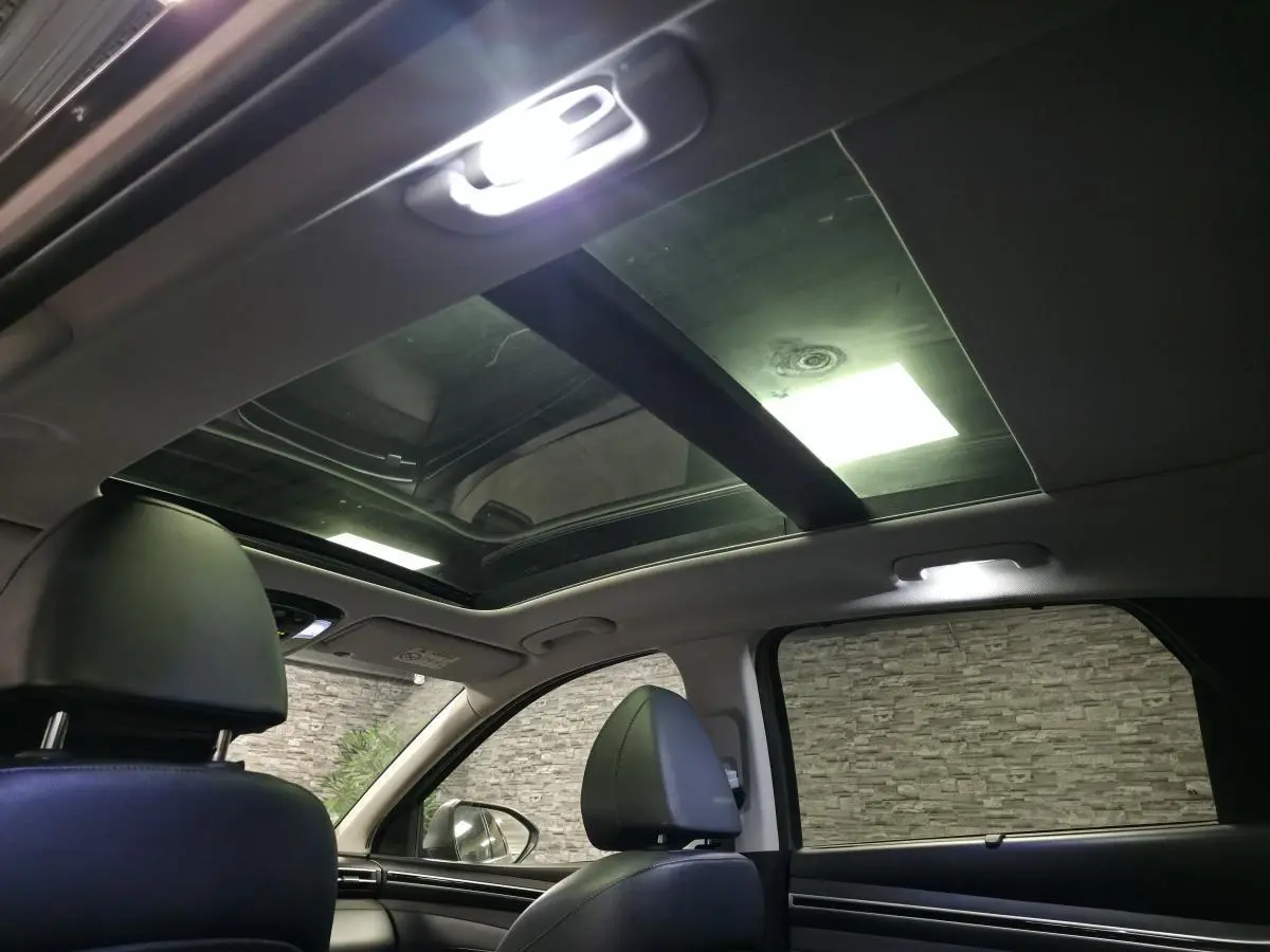 Vue intérieure du toit ouvrant panoramique et des sièges avant en cuir noir du Hyundai Tucson gris, avec éclairage intérieur allumé.
