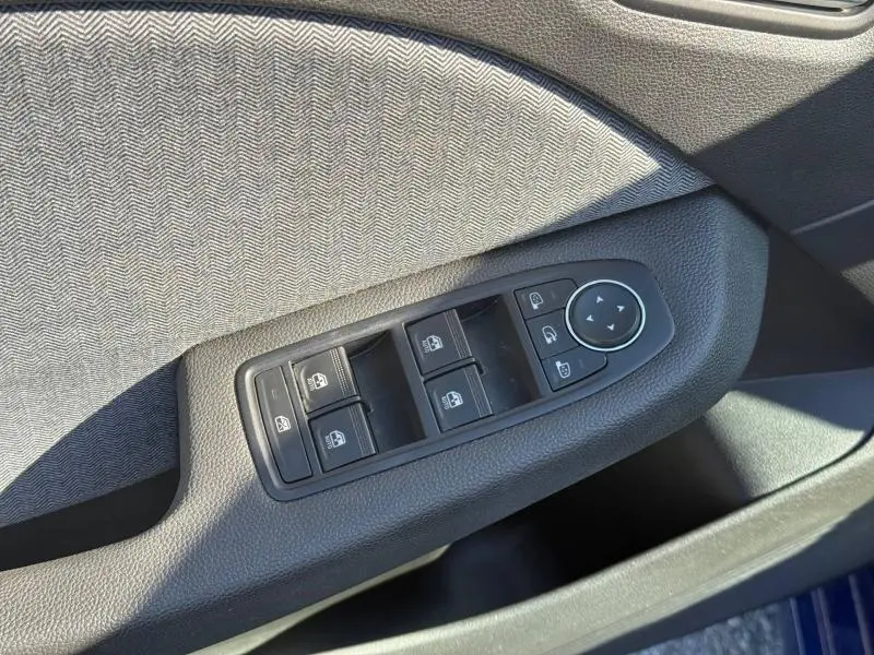 Gros plan sur les commandes des vitres et rétroviseurs côté conducteur de la Renault Clio 2025 Bleu Iron, tissu gris à motif chevrons.