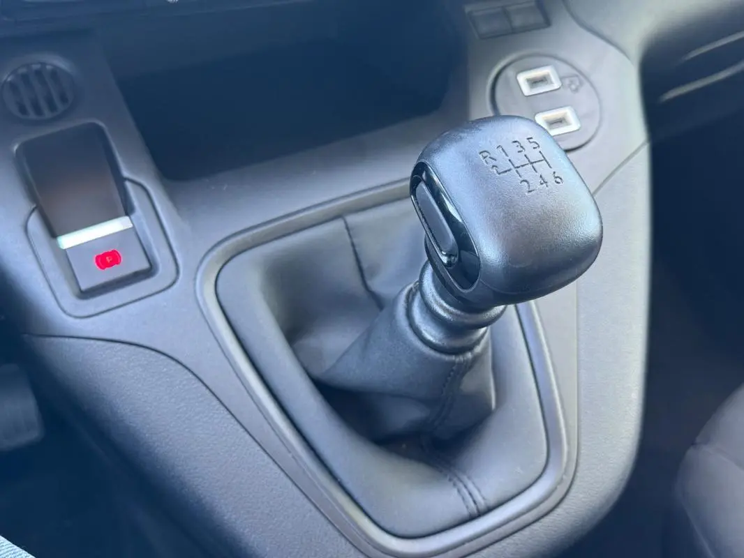 Gros plan sur le levier de vitesse manuel noir du Citroën Berlingo vert, avec frein à main électrique visible à gauche.