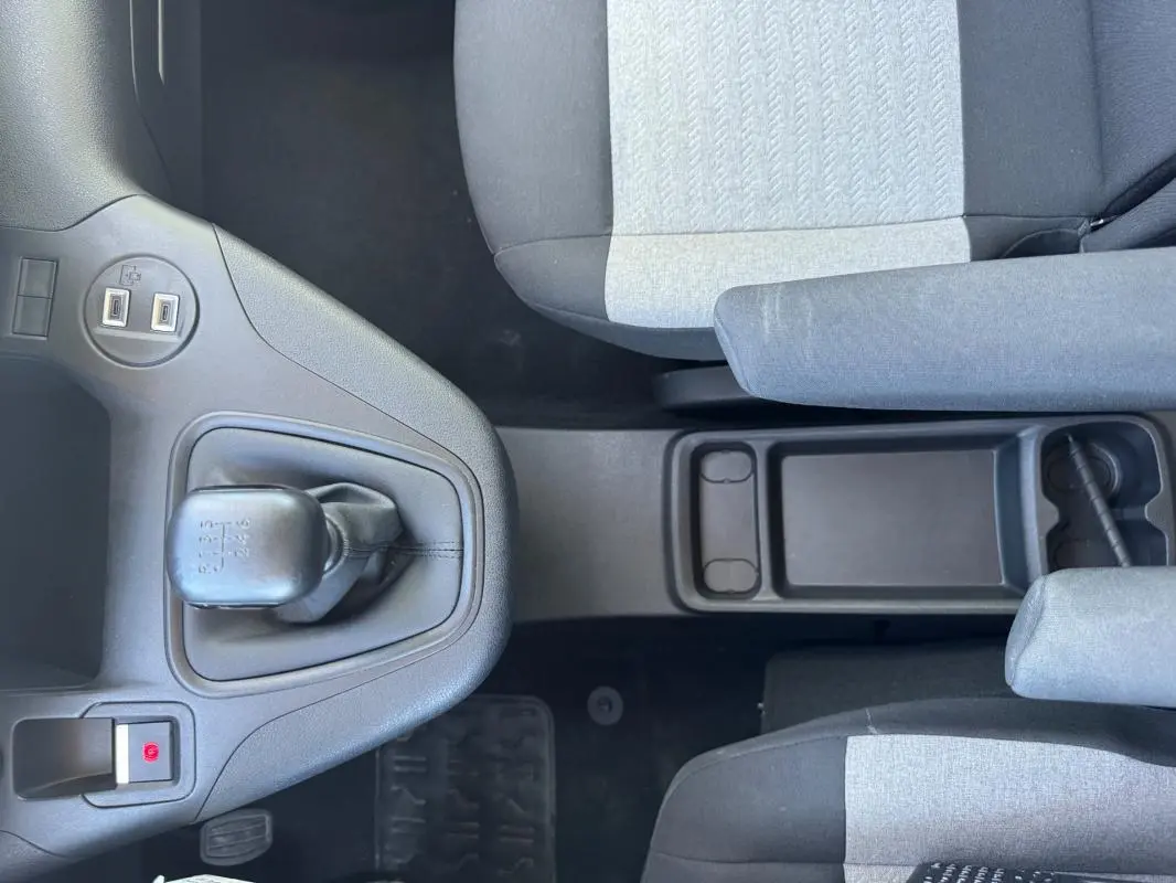 Vue intérieure centrée sur la console centrale et levier de vitesse manuel du Citroën Berlingo 2024, sièges gris et noirs.