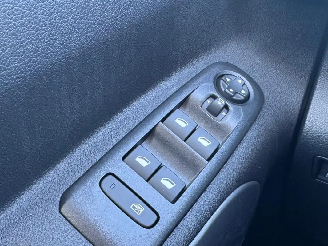 Gros plan sur les commandes des vitres électriques et des rétroviseurs côté conducteur d’un Citroën Berlingo vert 2024.