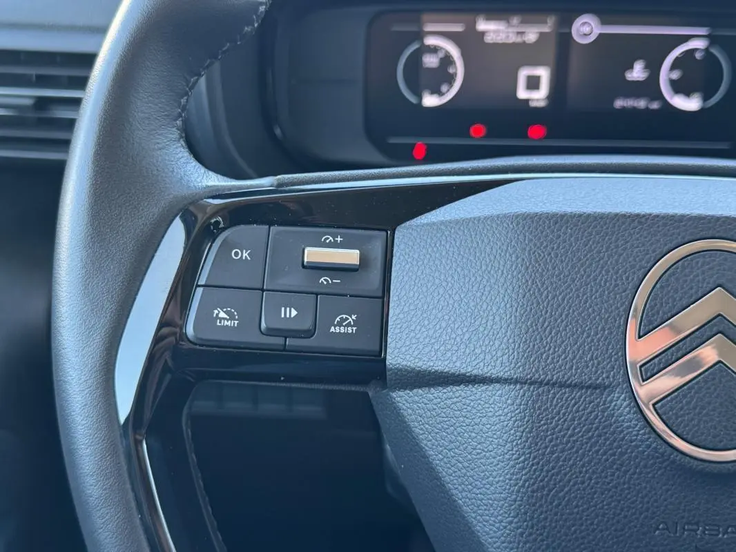 Gros plan sur le volant noir du Citroën Berlingo vert 2024, montrant les commandes de régulateur et limiteur de vitesse.