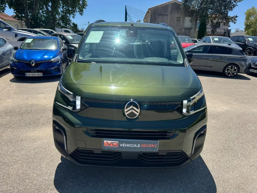 Vue avant d'un Citroën Berlingo vert métallisé avec barres de toit, sur un parking en plein jour.