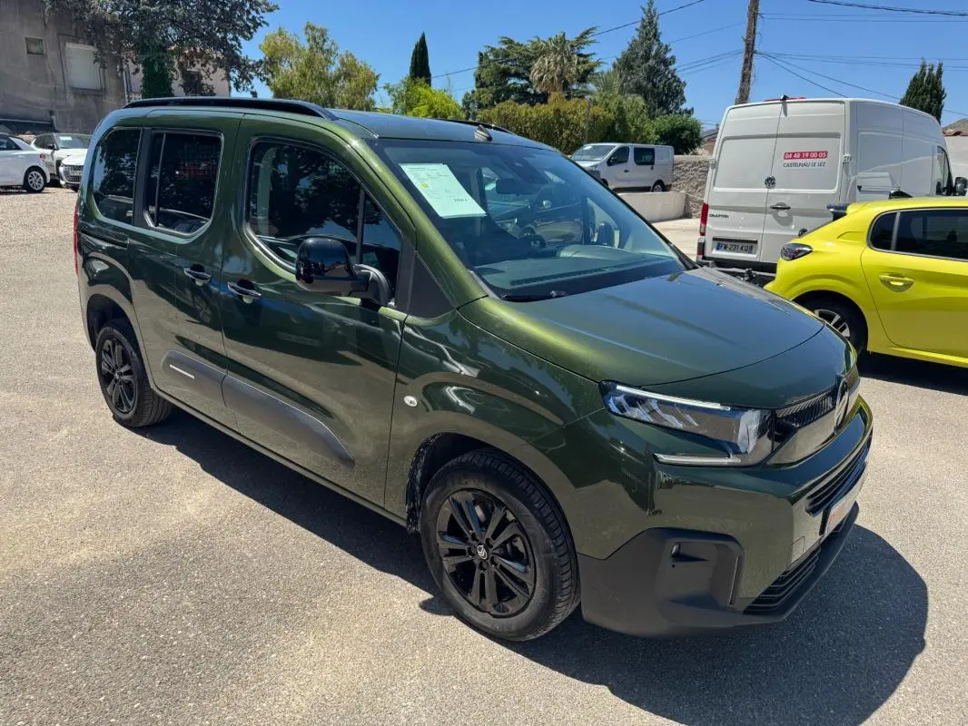 Vue 3/4 avant droit d'un Citroën Berlingo vert 2024 avec barres de toit et jantes noires.
