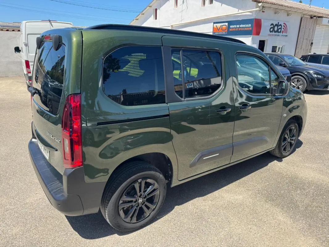 Vue 3/4 arrière droite d'un Citroën Berlingo vert 2024 avec barres de toit et vitres teintées.