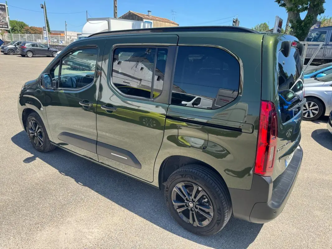 Vue 3/4 arrière droite d'un Citroën Berlingo vert 2024 avec barres de toit et vitres teintées.