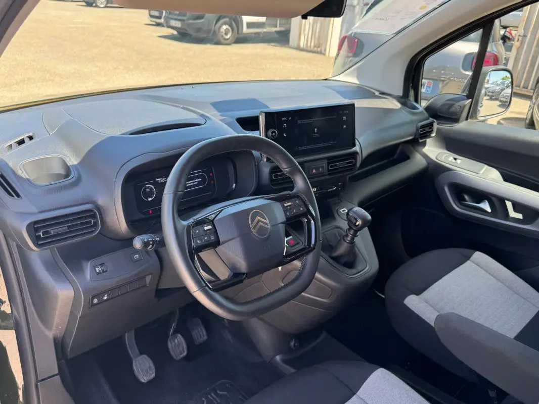 Vue intérieure côté conducteur du Citroën Berlingo 2024, tableau de bord noir avec écran central et volant multifonction.