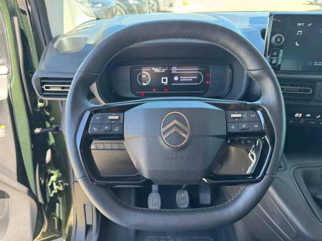 Vue rapprochée du volant noir du Citroën Berlingo vert 2024, avec commandes intégrées et tableau de bord numérique.