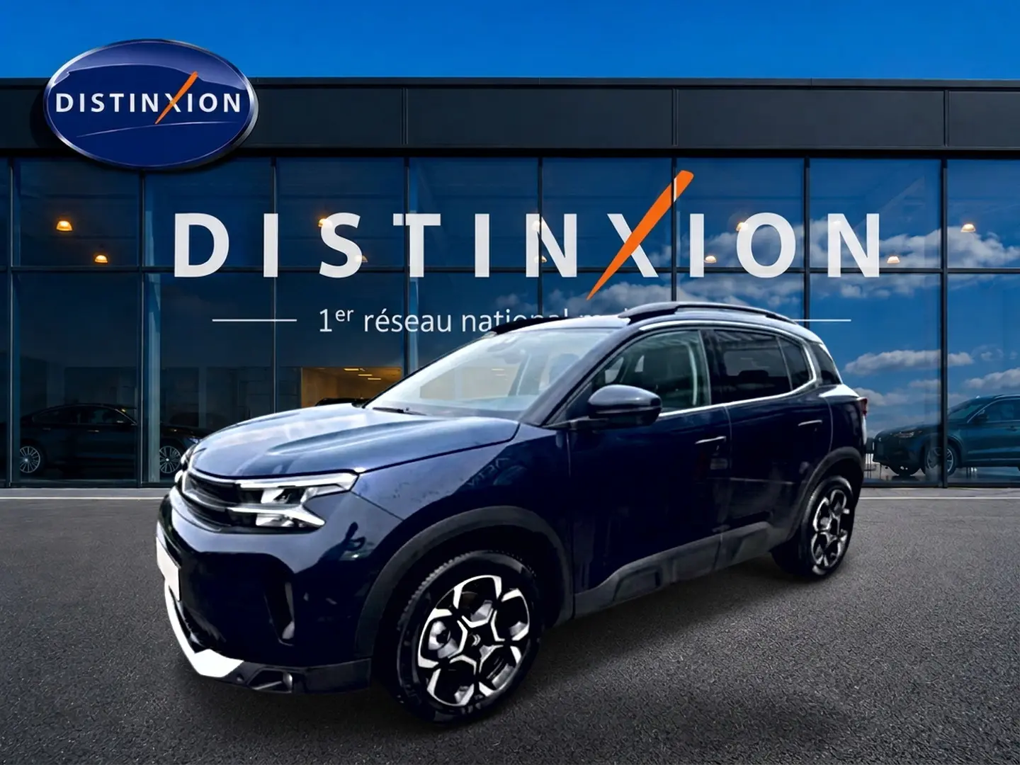 Vue 3/4 avant droite d'un Citroën C5 Aircross bleu eclipse avec jantes alu devant une vitrine Distinxion.