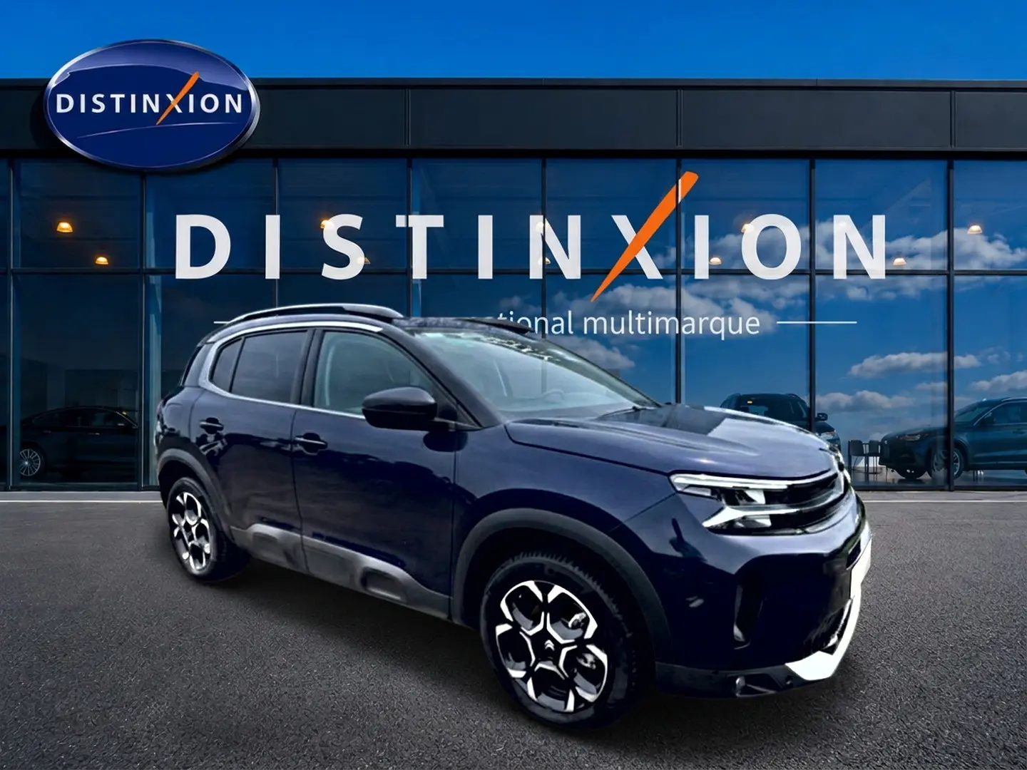 Citroën C5 Aircross bleu eclipse en 3/4 avant droit, avec jantes alu et barres de toit visibles devant vitrine Distinxion.