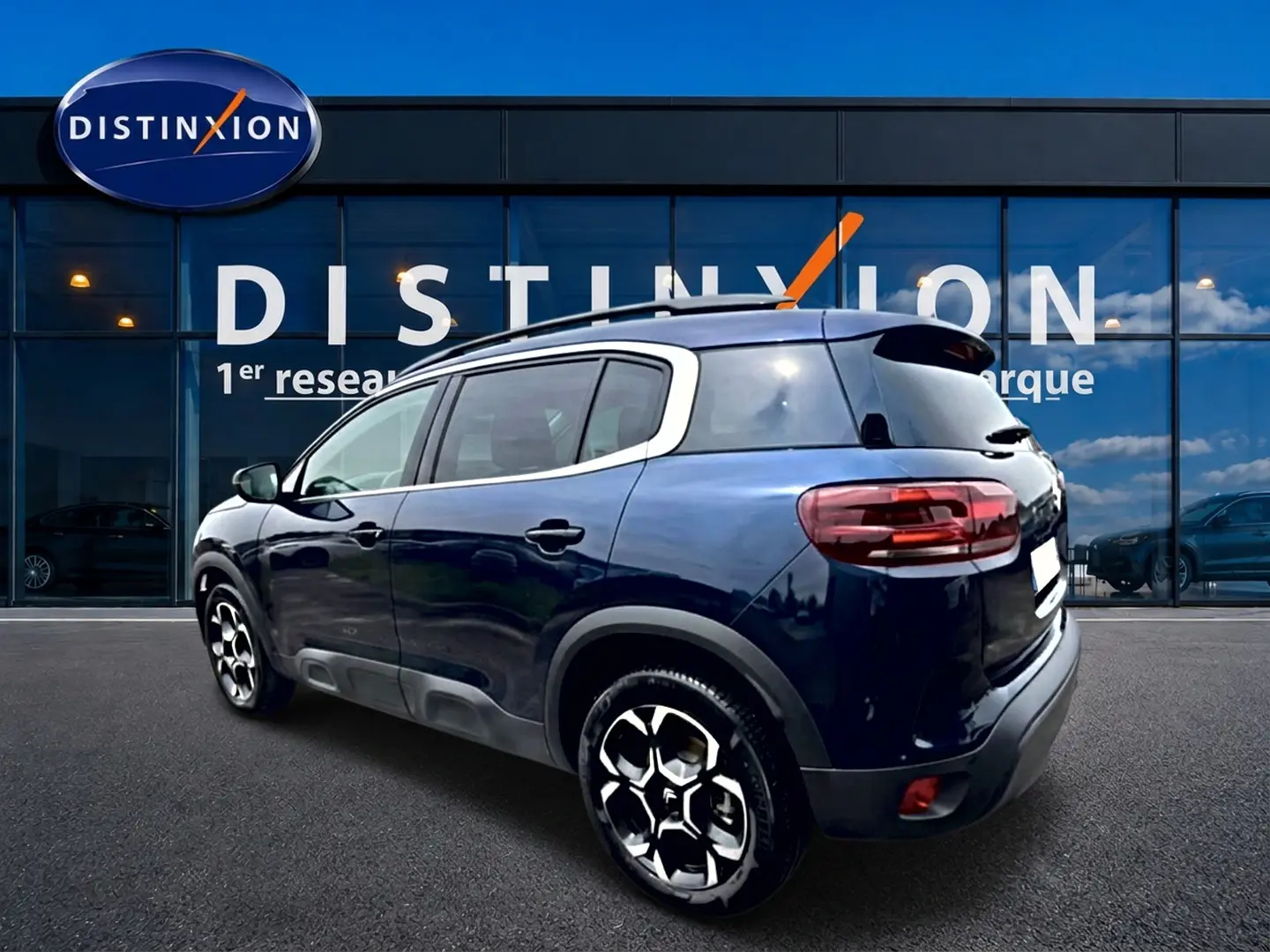 Vue 3/4 arrière droite d'un Citroën C5 Aircross bleu eclipse avec jantes alu et barres de toit visibles.