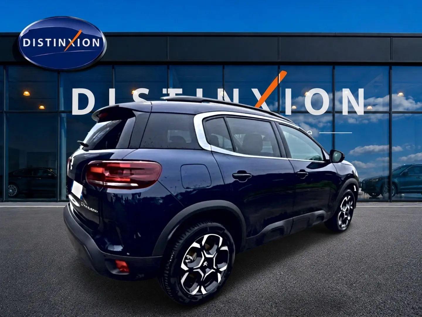 Vue 3/4 arrière droite d’un Citroën C5 Aircross bleu eclipse avec jantes alu et barres de toit visibles.