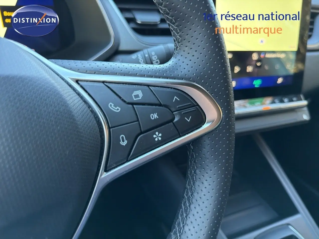 Gros plan sur le volant en cuir perforé avec commandes intégrées du Renault Symbioz gris Rafale, tableau de bord numérique en arrière-plan.