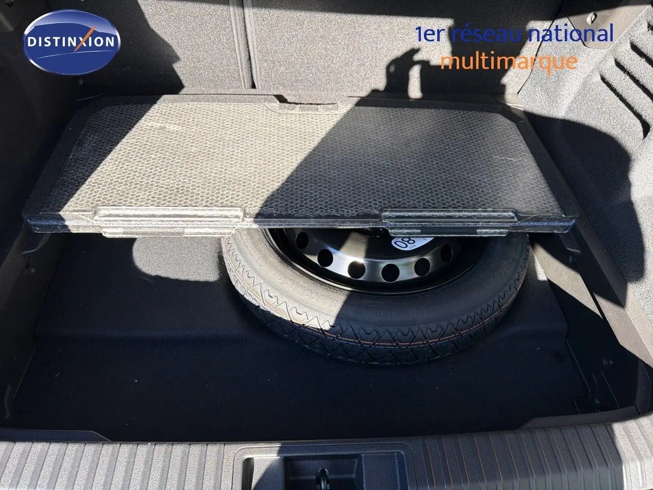Vue du coffre ouvert de la Renault Symbioz gris Rafale métal, montrant la roue de secours sous la tablette amovible.