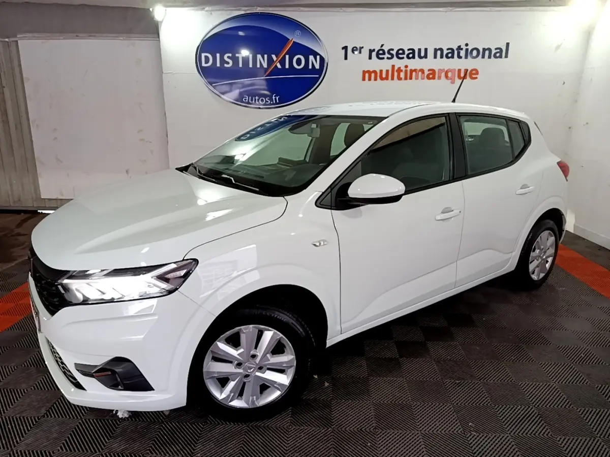 Vue 3/4 avant droite d'une Dacia Sandero Confort TCe 90 blanche, avec feux LED et jantes alliage visibles en intérieur showroom.