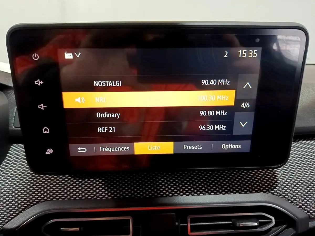 Écran tactile central affichant la liste des radios dans l’habitacle d’une Dacia Sandero blanche vue de face.