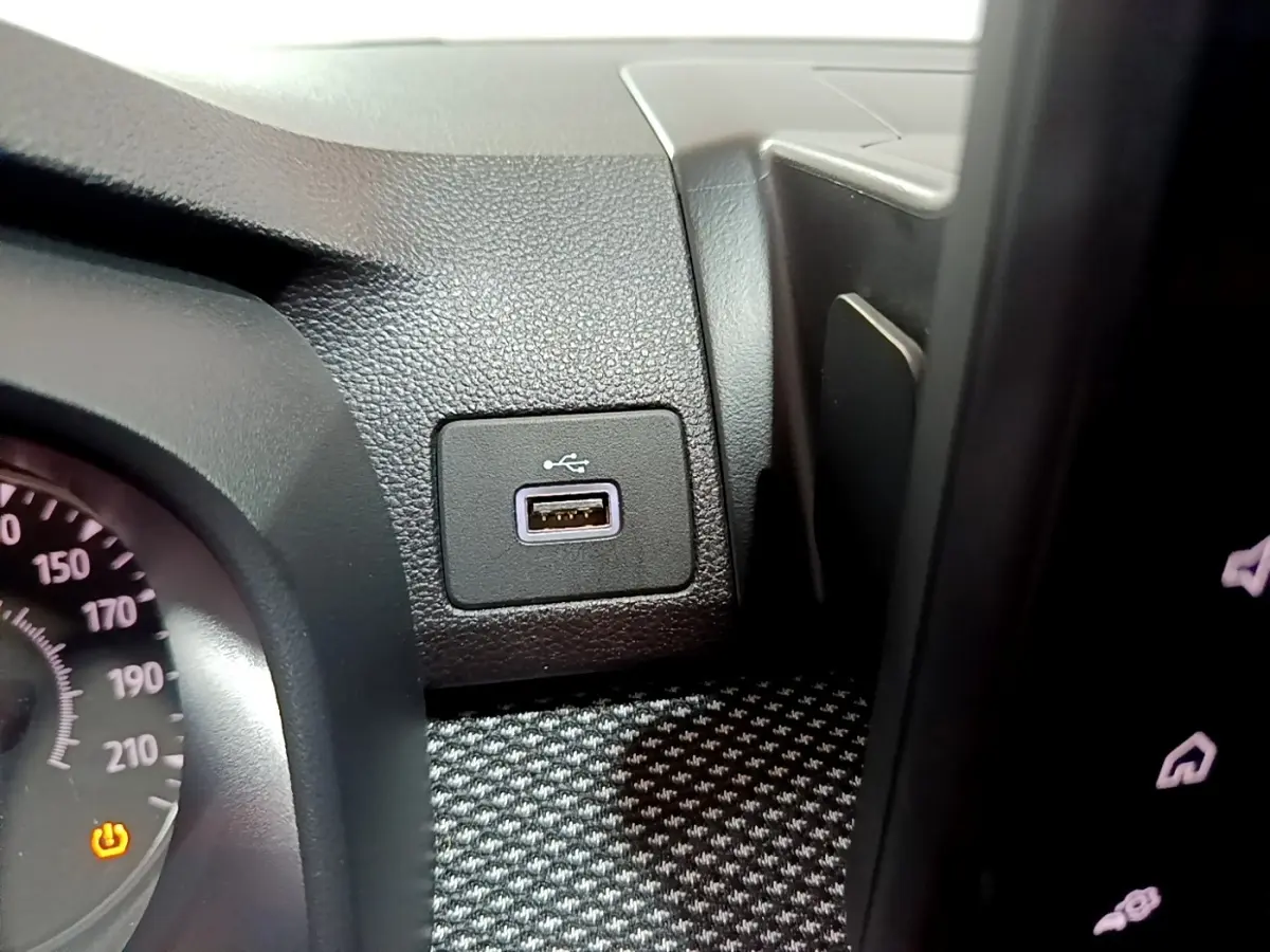 Gros plan intérieur sur la prise USB noire à côté du tableau de bord et du compteur de vitesse partiel de la Dacia Sandero blanche.