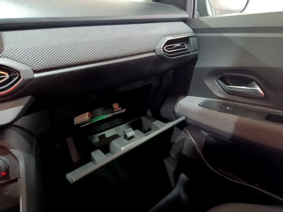 Intérieur de la Dacia Sandero Confort TCe 90 2022, vue côté passager avec boîte à gants ouverte et garnitures texturées noires.