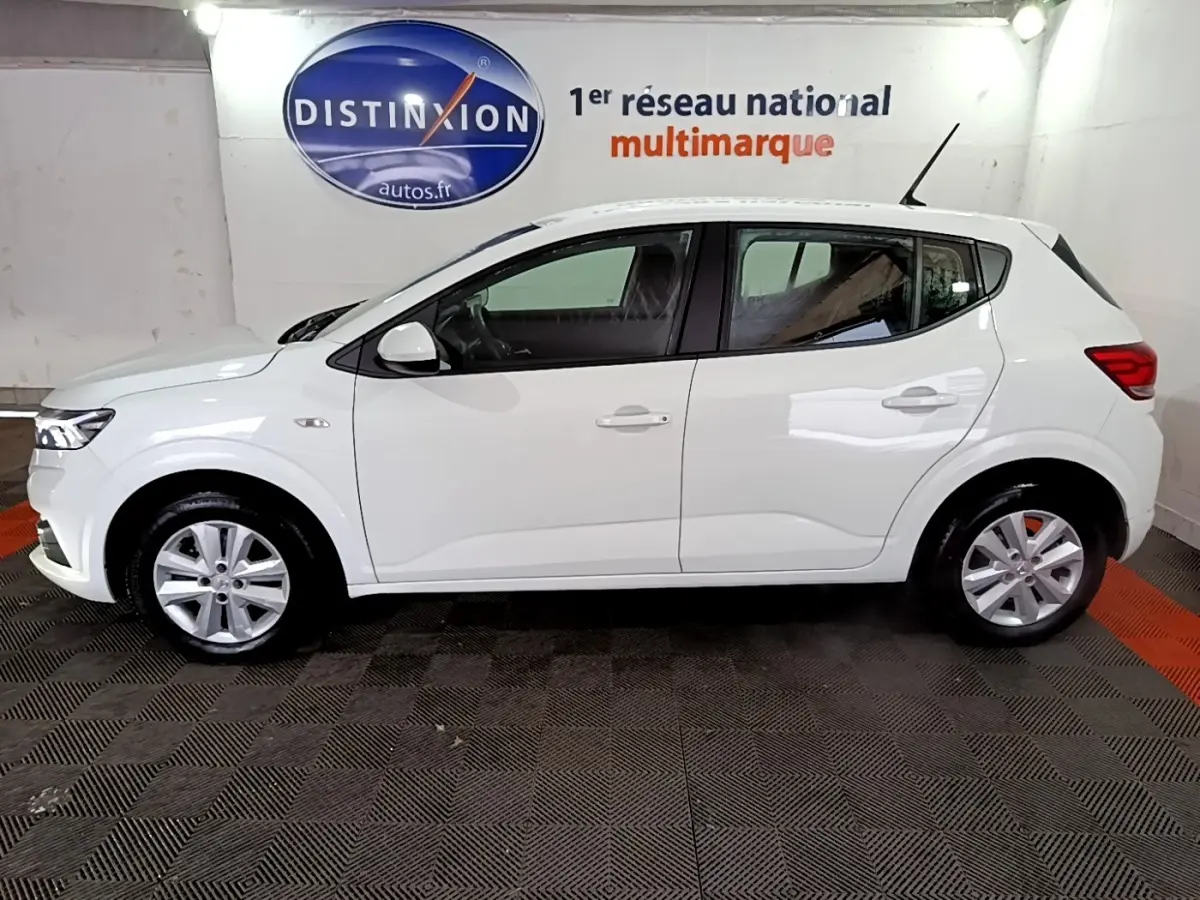 Vue de profil côté gauche d'une Dacia Sandero blanche 2022, finition Confort, dans un showroom intérieur.
