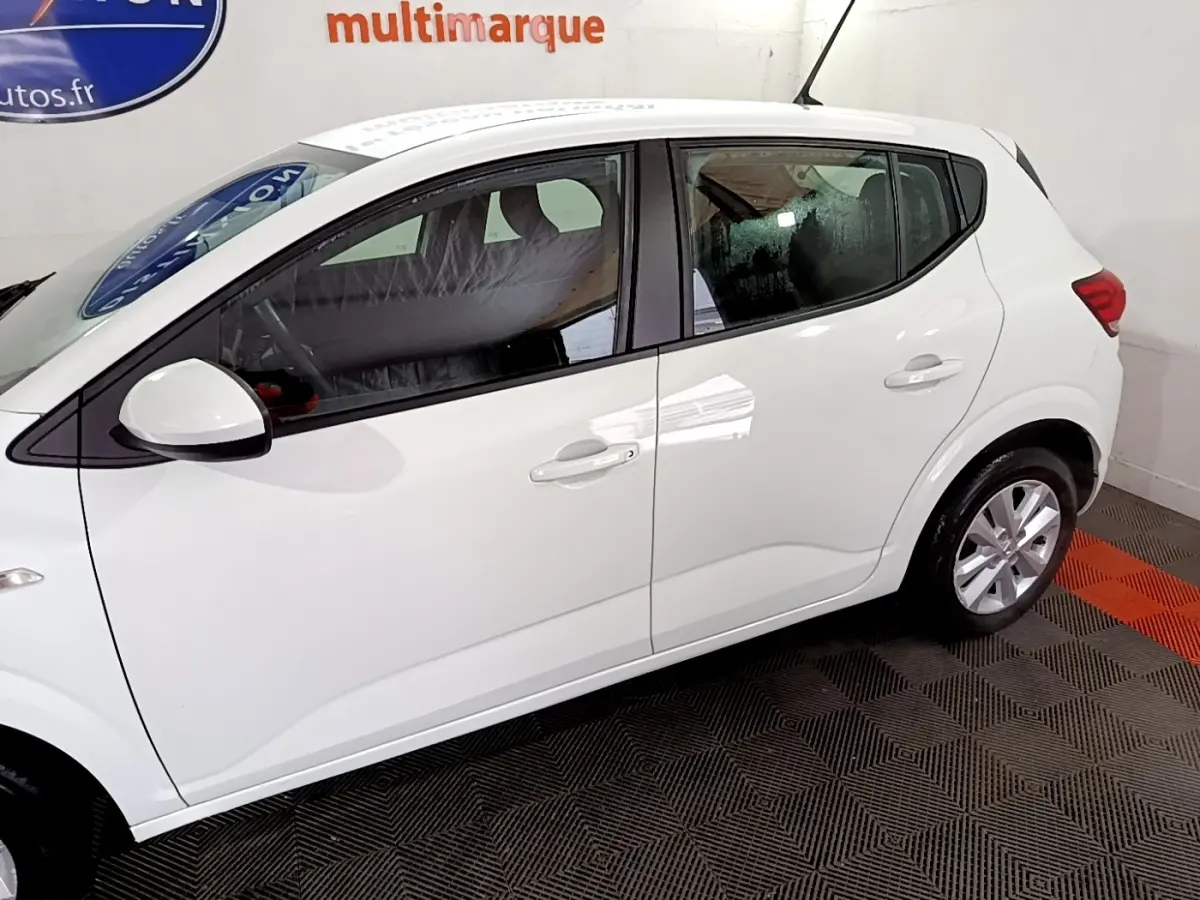 Vue de profil côté gauche d'une Dacia Sandero blanche 2022, avec poignées de porte et rétroviseur assortis.