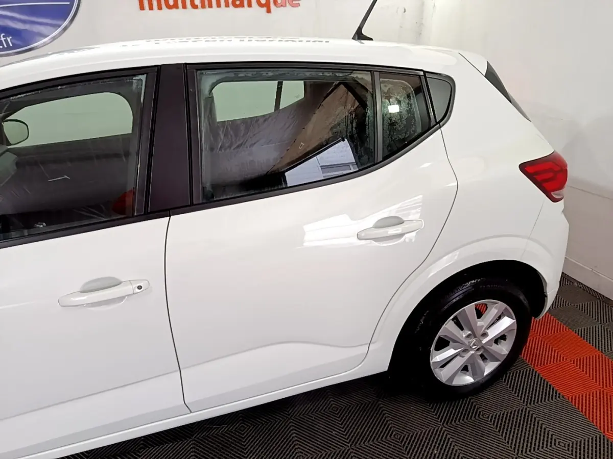 Vue latérale côté droit d'une Dacia Sandero blanche 2022, mettant en valeur les portes arrière et la roue arrière.