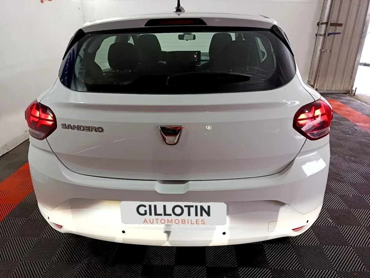 Vue arrière d'une Dacia Sandero blanche 2022 avec feux LED allumés dans un garage fermé.