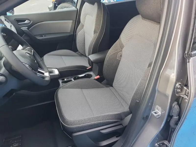 Vue intérieure côté conducteur du Renault Captur gris Cassiopée, sièges tissu gris avec accoudoir central et volant multifonction.