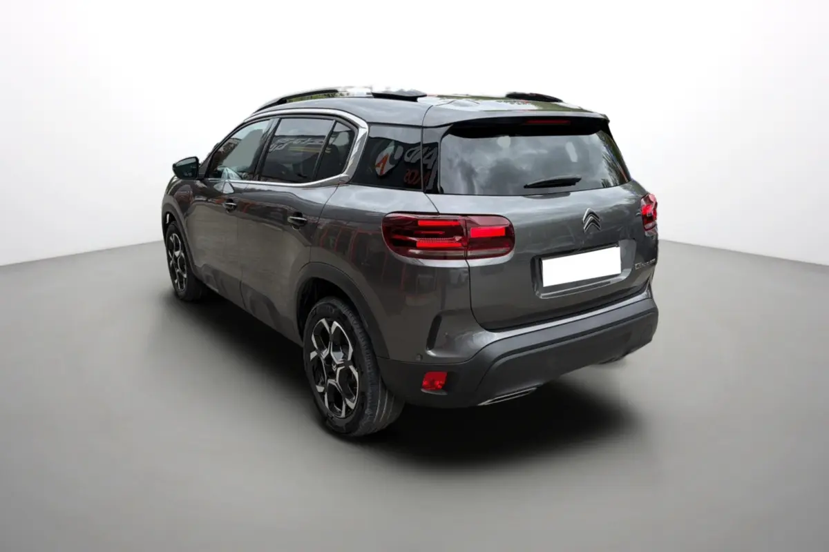 Vue 3/4 arrière gauche d'un Citroën C5 Aircross Hybrid gris platinium avec barres de toit et vitres surteintées.