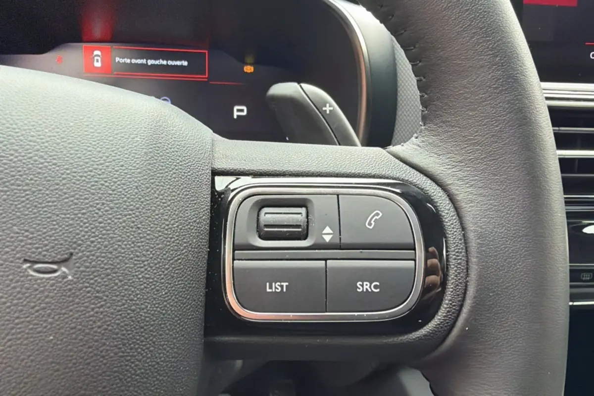 Gros plan sur les commandes multifonctions du volant cuir du Citroën C5 Aircross Hybrid 2025, finition gris platinium.