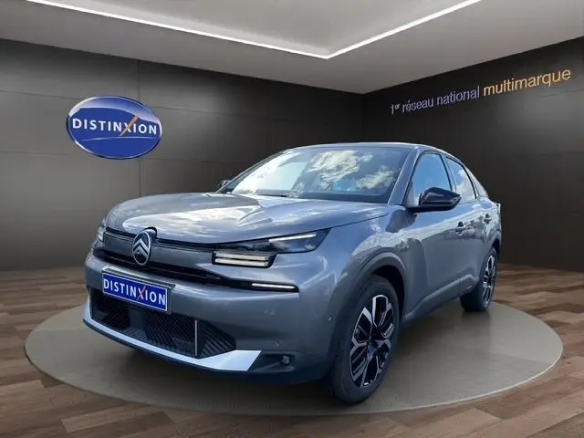Vue 3/4 avant d'une Citroën C4 hybride gris clair avec jantes noires et détails chromés, sur podium intérieur.