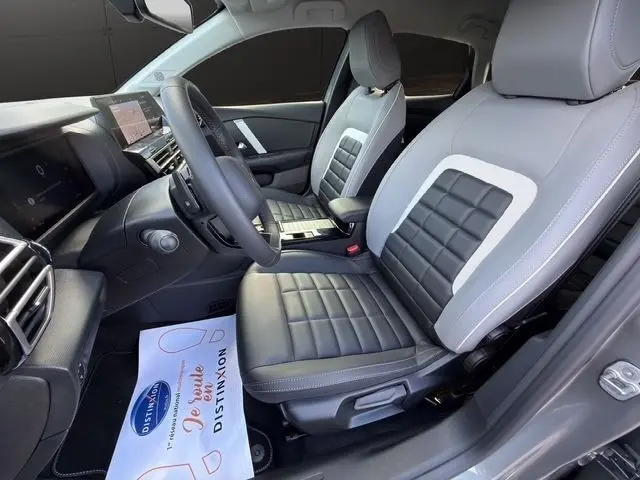 Vue intérieure côté conducteur de la Citroën C4 hybride 2025, sièges cuir bicolores gris et noir avec tableau de bord digital.