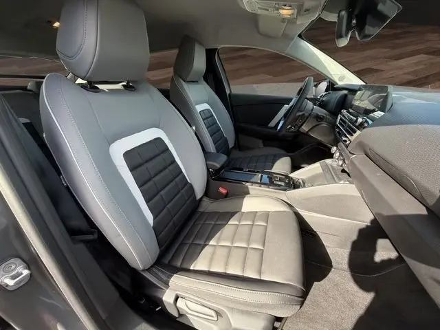 Vue intérieure côté gauche de la Citroën C4 hybride 2025, sièges bi-ton gris clair et noir avec console centrale moderne.