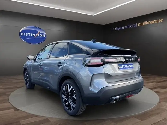 Vue 3/4 arrière droite d'une Citroën C4 hybride gris clair avec jantes noires et toit noir dans un showroom.