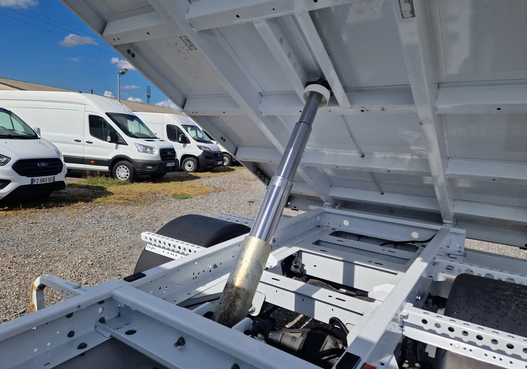 Vue rapprochée sous la benne relevée d’un Renault Master blanc, mettant en valeur le vérin hydraulique et le châssis.