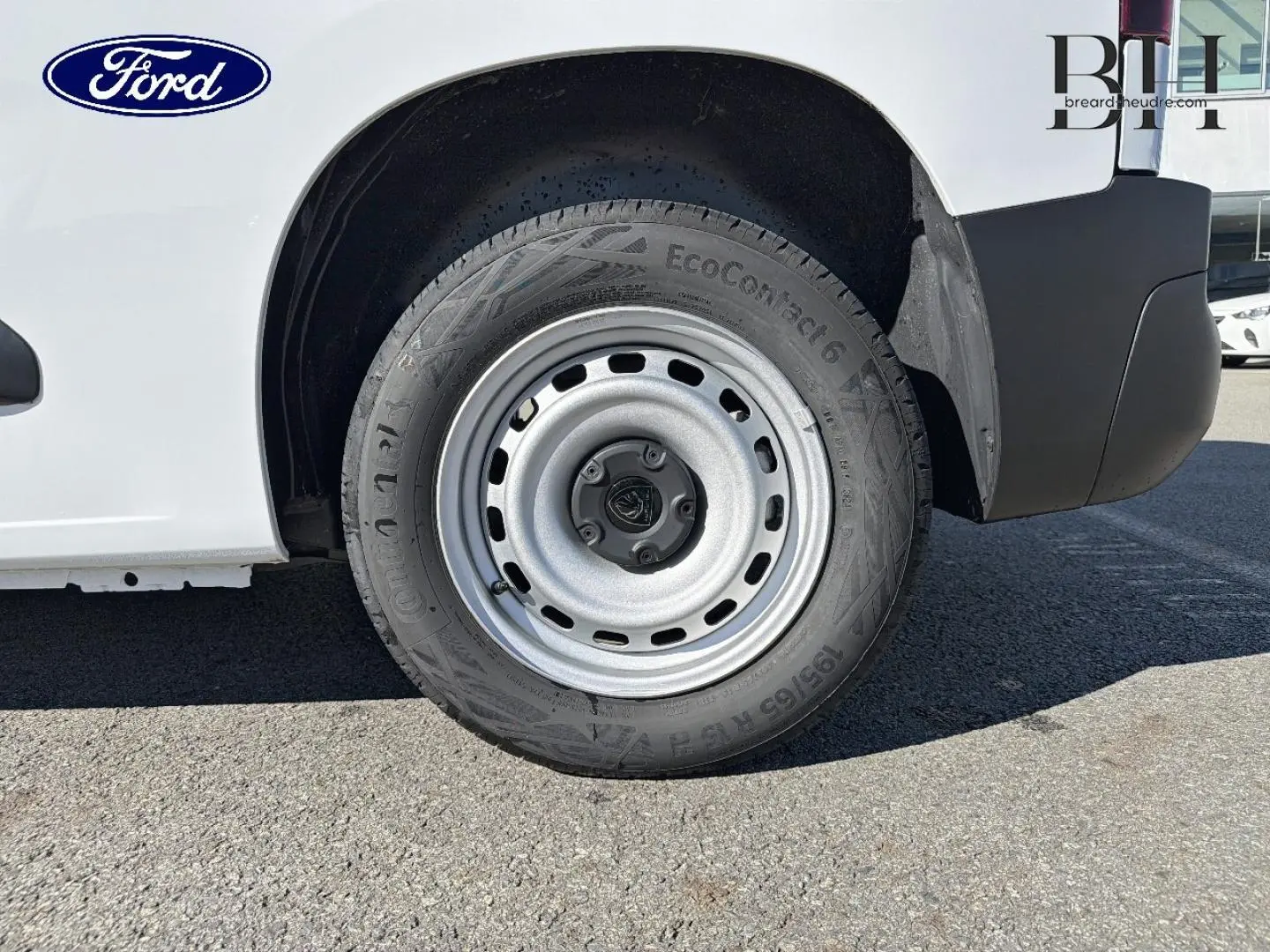 Gros plan sur la roue arrière droite d’un utilitaire blanc avec jante acier et logo Ford visible.