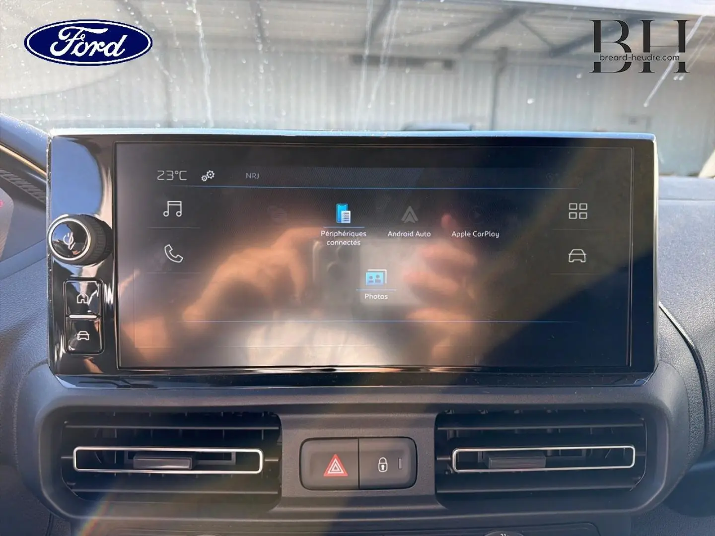 Écran tactile central du tableau de bord d’un Peugeot Partner blanc, avec commandes et aérateurs visibles.