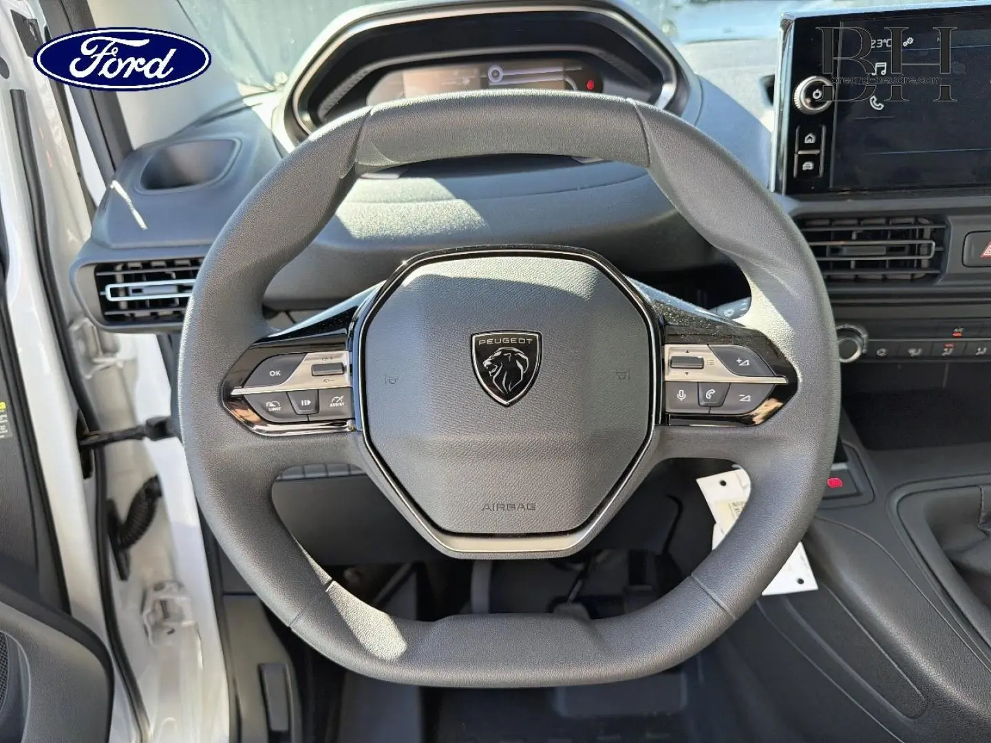 Vue intérieure centrée sur le volant Peugeot noir avec logo lion, tableau de bord et écran tactile en arrière-plan.