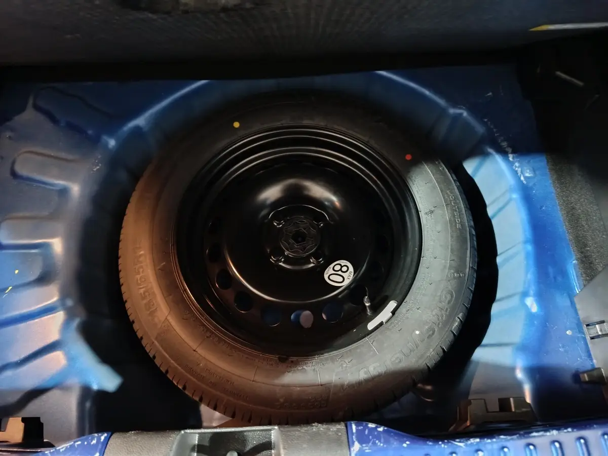 Roue de secours galette en jante acier noir dans le coffre bleu d'une Dacia Sandero Extreme+ TCe 110 2024.