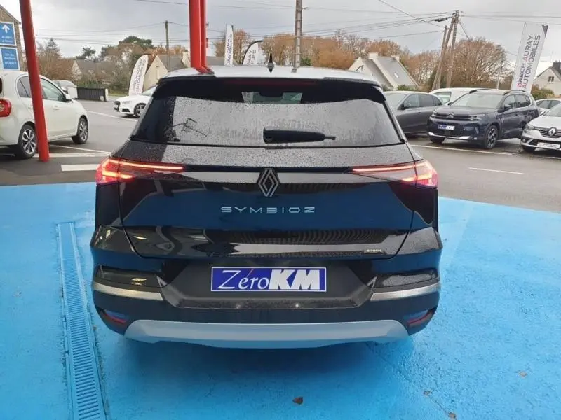 Vue arrière d'une Renault SYMBIOZ noir étoilé avec feux arrière LED allumés sur parking extérieur.