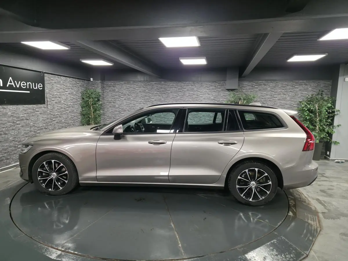Vue de profil côté gauche d'une Volvo V60 gris métallisé avec jantes alliage 17 pouces en intérieur showroom.