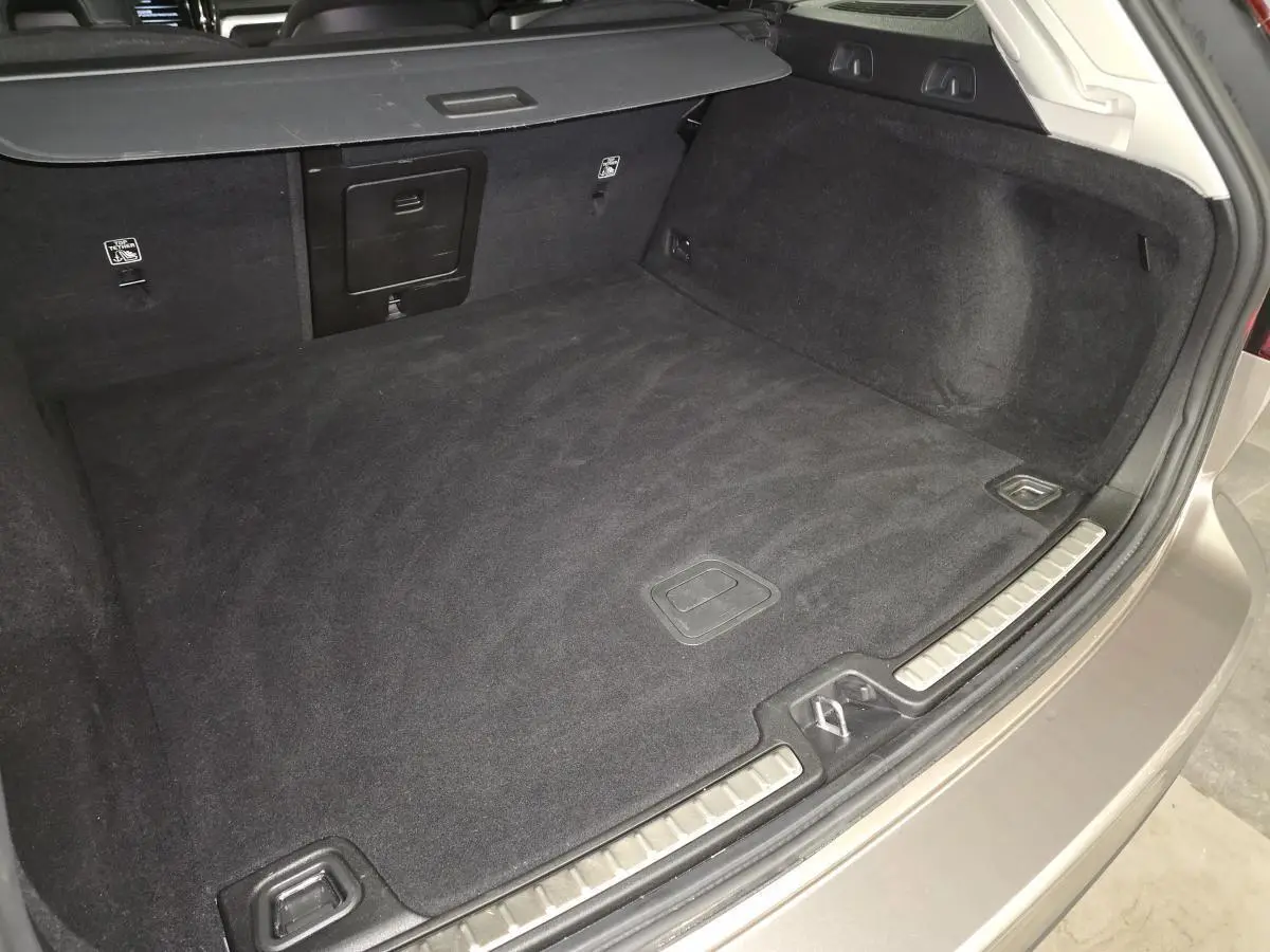 Coffre spacieux gris d'une Volvo V60 B4 Momentum Essentiel 2021, vue intérieure arrière avec tapis noir.