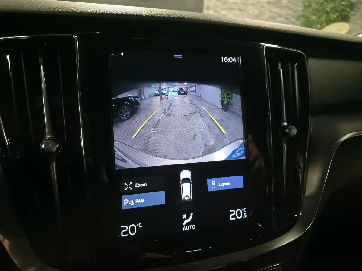 Écran tactile intérieur montrant la caméra de recul d'une Volvo V60 gris, avec lignes de guidage jaunes visibles.